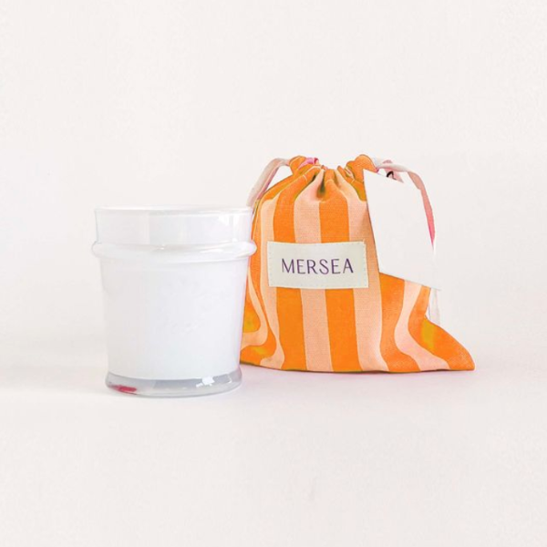 Candle in a glass jar with a striped drawstring bag labeled 'MERSEA' on a white background