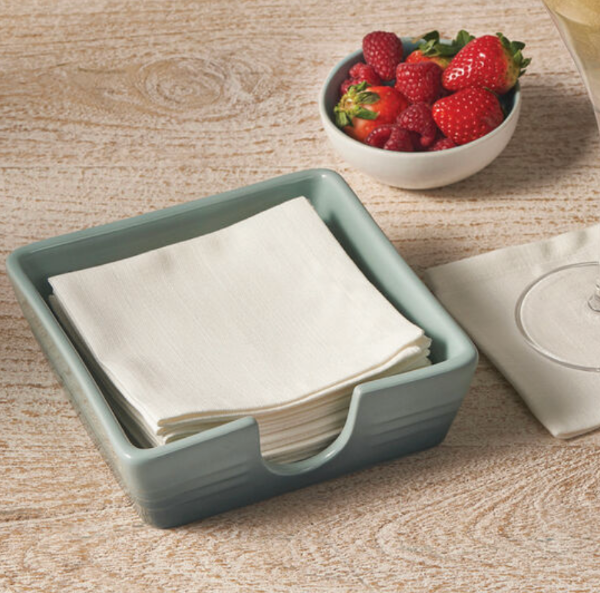 Napkin holder with folded napkins next to a bowl of strawberries on a wooden surface