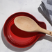Red Le Creuset spoon rest with a wooden spoon on a light gray background