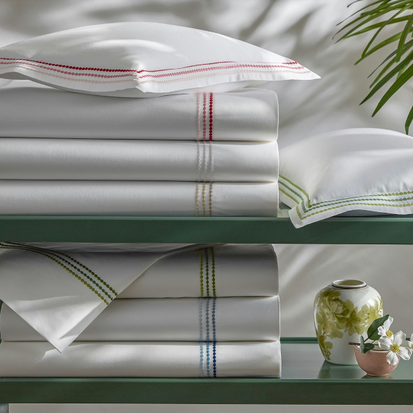 Stack of white bed sheets with decorative stripes on a green table with a plant in the background