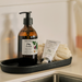 Osmology Fig Leaf hand wash and soap on a black tray by a sink.