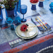 Decorative table setting with blue glasses, gold cutlery, and a floral centerpiece on a patterned tablecloth.