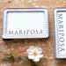 Two white picture frames with 'Mariposa' branding on a wooden surface with a white flower.