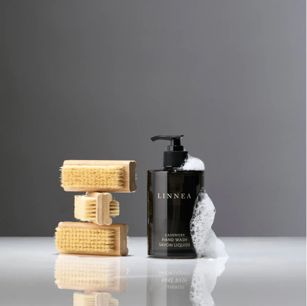 LINNEA hand wash bottle with sponges on a reflective surface against a gray background