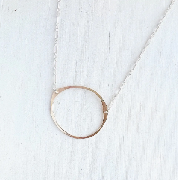 Gold circular pendant necklace on a white textured background