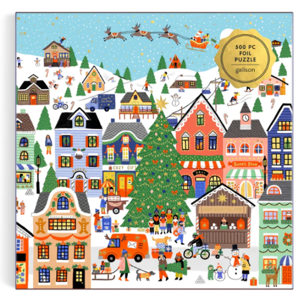 A 500-piece foil puzzle featuring a colorful, whimsical winter village scene with houses, a Christmas tree, sleigh, and festive people. The puzzle box has a gold circular badge in the top right that reads '500 PC FOIL PUZZLE galion'.
