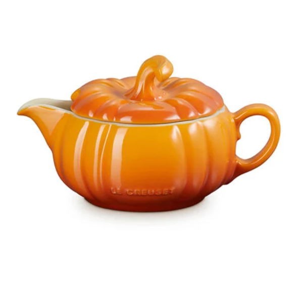 An orange pumpkin-shaped ceramic teapot with a matching lid, featuring the Le Creuset brand name embossed on the front, set against a plain white background.