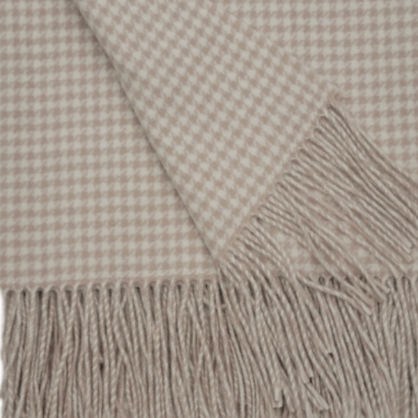 A close-up of a woven throw blanket with a beige and off-white houndstooth pattern and fringed edges.