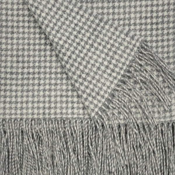 Close-up of a gray and off-white houndstooth patterned throw blanket with fringed edges.