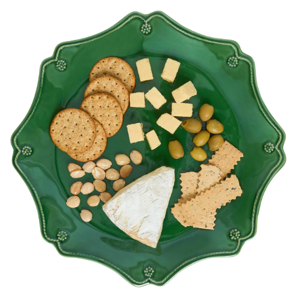 A green scalloped ceramic plate with decorative raised edges, filled with an appetizer spread including crackers, cubed cheese, a wedge of soft cheese, sliced crackers, peanuts, and green olives, isolated on a white background.