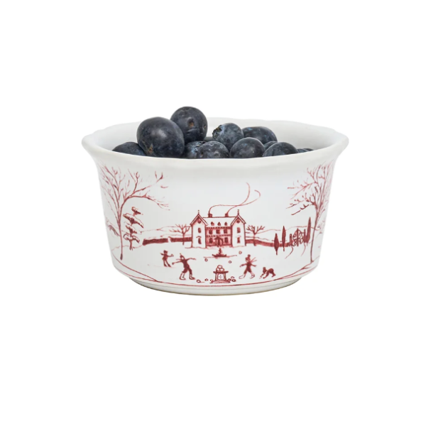 A white ceramic bowl with a red winter landscape print, filled with blueberries, on a solid white background.