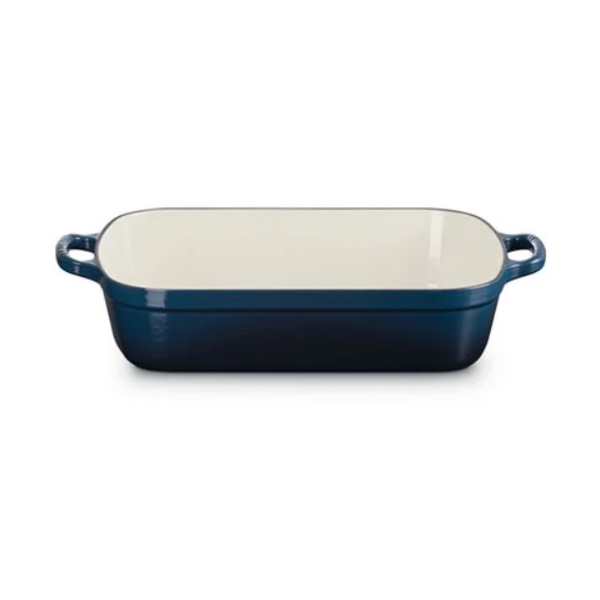 A rectangular enameled baking dish with a dark blue exterior and a cream-colored interior, featuring side handles, shown on a plain white background.