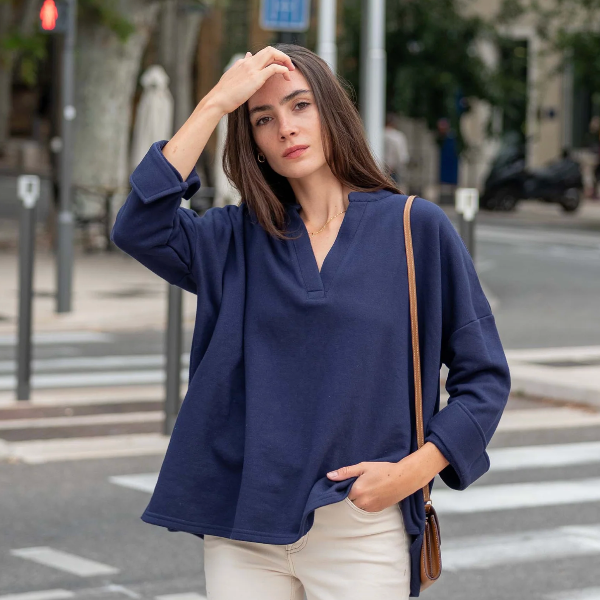 A woman wearing an oversized navy blue V-neck long-sleeve top and cream pants, standing on a city street crosswalk with a brown shoulder bag.