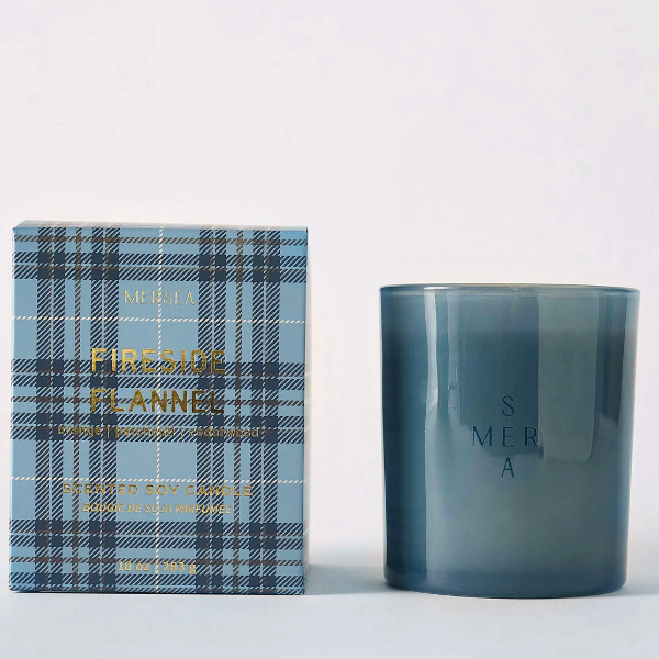 A candle product shown with its retail box and the candle vessel itself on a clean white background. The box is light blue plaid with gold lettering reading 'FIRESTRIKE FLANNY' and 'FRESH SEA SALT WOOD SPICE'.