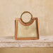 Woven handbag with leather handle on a wooden surface and beige background