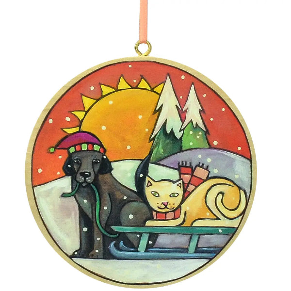 Decorative ornament with a dog and cat on a sled under a sun and trees.