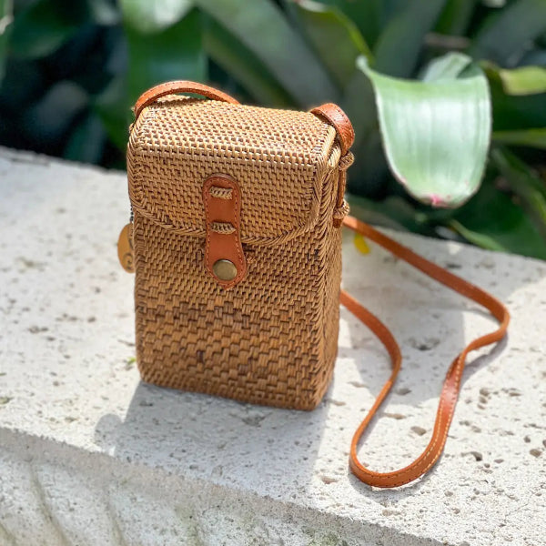 Woven handbag with leather strap on a stone surface with green foliage in the background