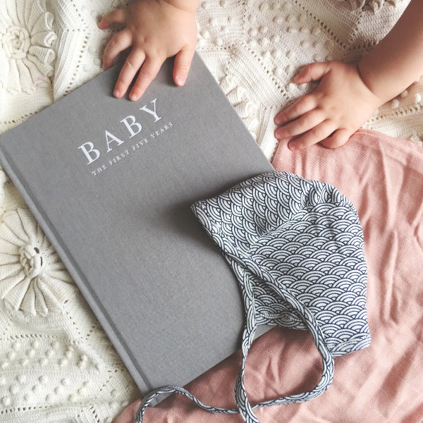 Gray book titled 'BABY' with baby clothes on a textured surface