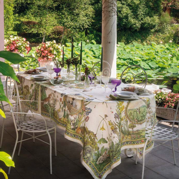 Outdoor dining table set with a decorative tablecloth on a patio with greenery.