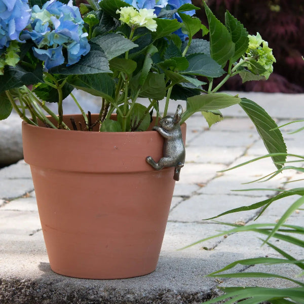 Terracotta pot with hydrangeas and a metal rabbit ornament on a stone surface.