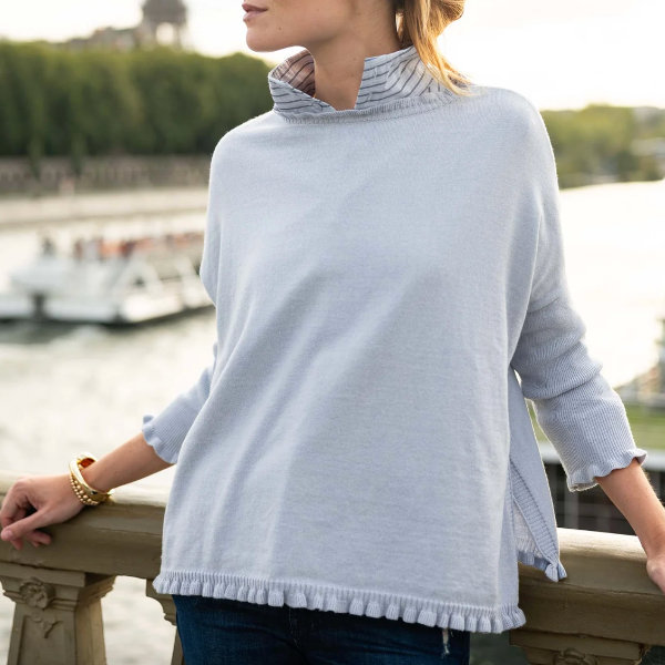 Person wearing a light blue sweater with a blurred background of water and greenery