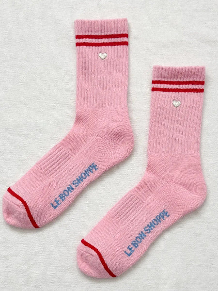 Pink socks with red stripes and heart designs on a light gray background
