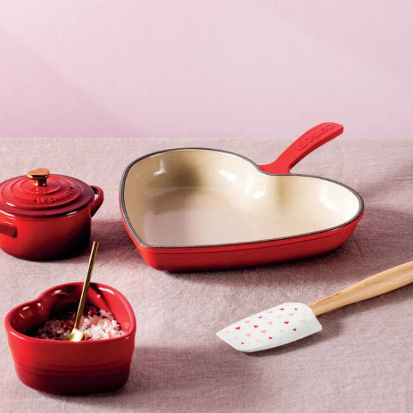 Red heart-shaped cookware set on a pink background
