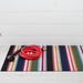 Striped doormat with a coiled red garden hose on a white wooden floor.