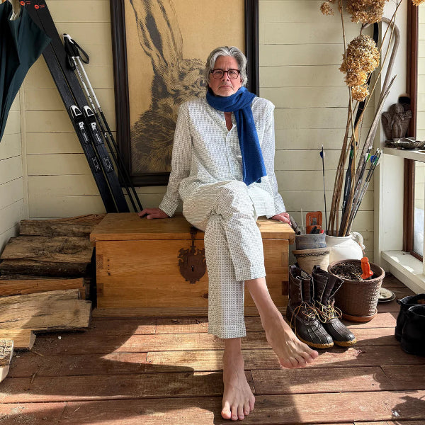 Person sitting on a wooden box in a rustic room with tools and plants.