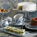 Tea set with finger sandwiches, a cake, and other pastries on a table with decorative wallpaper.