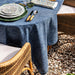 Dining table set with blue tablecloth, plates, and cutlery outdoors on a gravel surface.