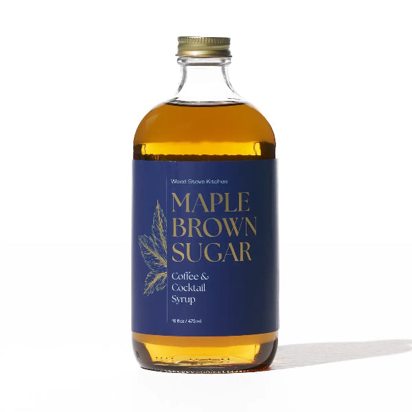 A bottle of Wood Stove Kitchen Maple Brown Sugar coffee and cocktail syrup, featuring a dark blue label with gold lettering and a gold cap, set against a plain white background.