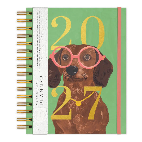 A spiral-bound 2027 dachshund planner by Seedings, featuring a brown dachshund wearing pink glasses and gold-framed glasses on a mint green cover with gold foil numbers.