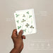 Hand holding a plantable seed paper envelope with clover design on a beige background