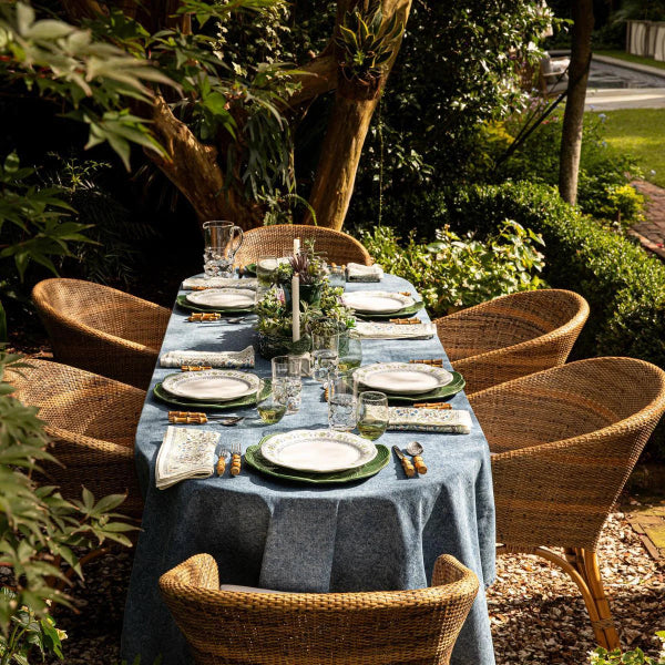Dining table set for a meal outdoors with chairs and a blue tablecloth.