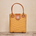 Wicker handbag with brown leather handles and accents on a wooden surface.