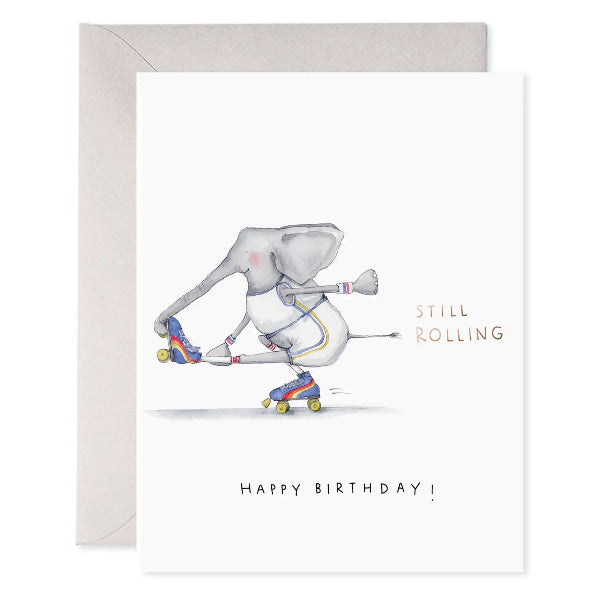 A white birthday card with a watercolor illustration of an elephant roller skating, alongside a light gray envelope. The card features the text 'STILL ROLLING' and 'HAPPY BIRTHDAY!' in black and gold lettering.