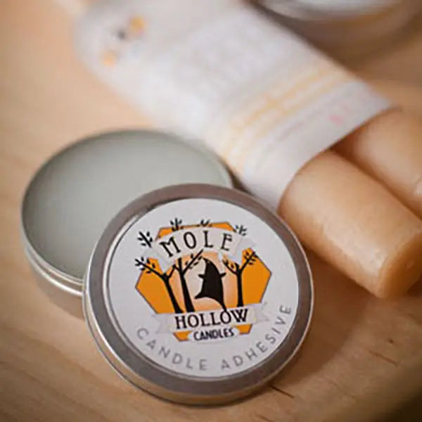 A round metal tin of candle adhesive with its lid off, showing the pale wax inside. The front label reads 'Mole Hollow Candles' with a black mouse on a hill graphic.
