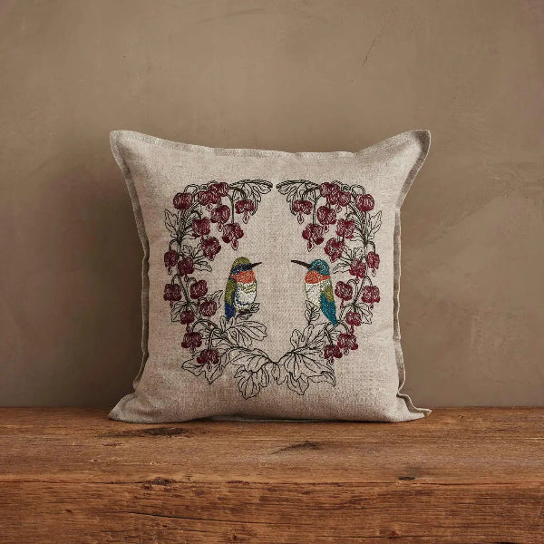Decorative pillow with bird and floral design on a wooden surface and beige background