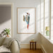A framed art print of a colorful spotted bird perched on a branch, displayed on a white wall in a bright, modern living room with a sofa, side table, and window.