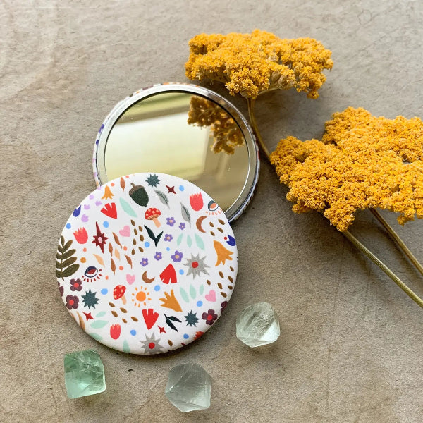 Compact mirror with floral design on a textured surface with yellow flowers and crystals.