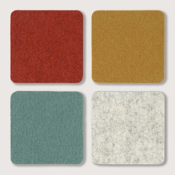 Four square felt-like material swatches arranged in a 2x2 grid on a light gray background: red, mustard yellow, muted teal, and off-white with subtle gray marbling.