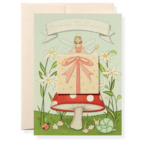 Greeting card with a fairy on a mushroom holding a gift box, surrounded by flowers and plants.