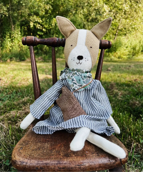 Stuffed animal dog in a dress sitting on a wooden chair outdoors.