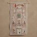 A vertical woven wall hanging tapestry featuring a detailed multi-story building facade with windows, figures, and decorative motifs, suspended from a light wood rod against a plain beige wall.