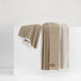 A folded beige throw blanket draped over a white display block against a clean white background.