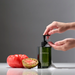 Person using LINNEA hand soap with a tomato and watermelon on a gray background