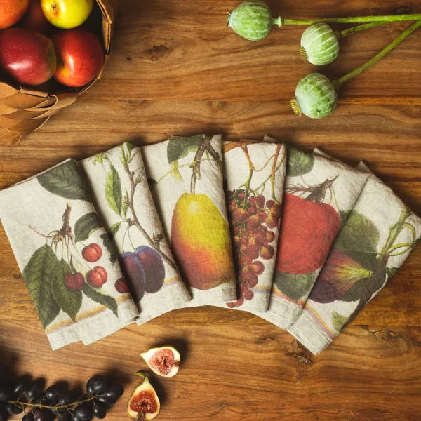 A set of folded linen napkins with a vintage fruit and berry print, arranged in a fan shape on a rustic wooden table with decorative fruit props.