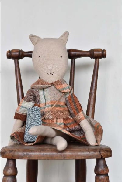 Stuffed animal cat wearing a plaid coat sitting on a wooden chair against a white background