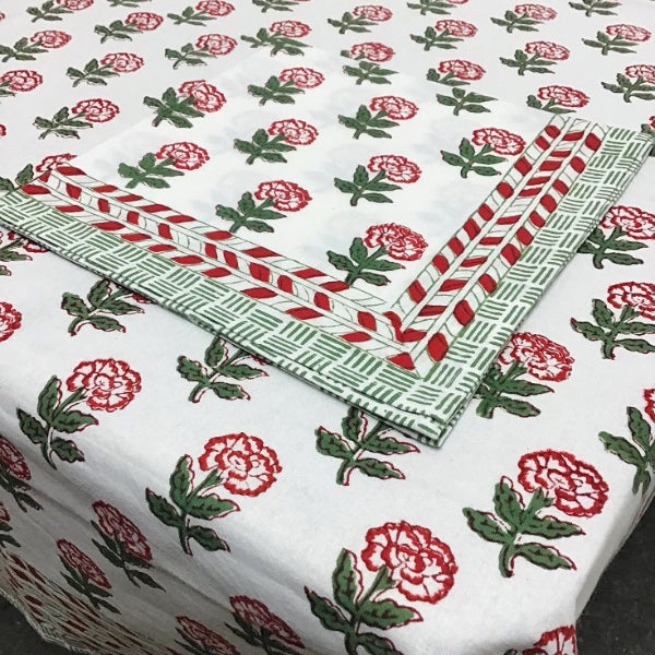 A white cotton tablecloth with a red and green floral block print pattern and a matching folded corner showing a red and green geometric border.
